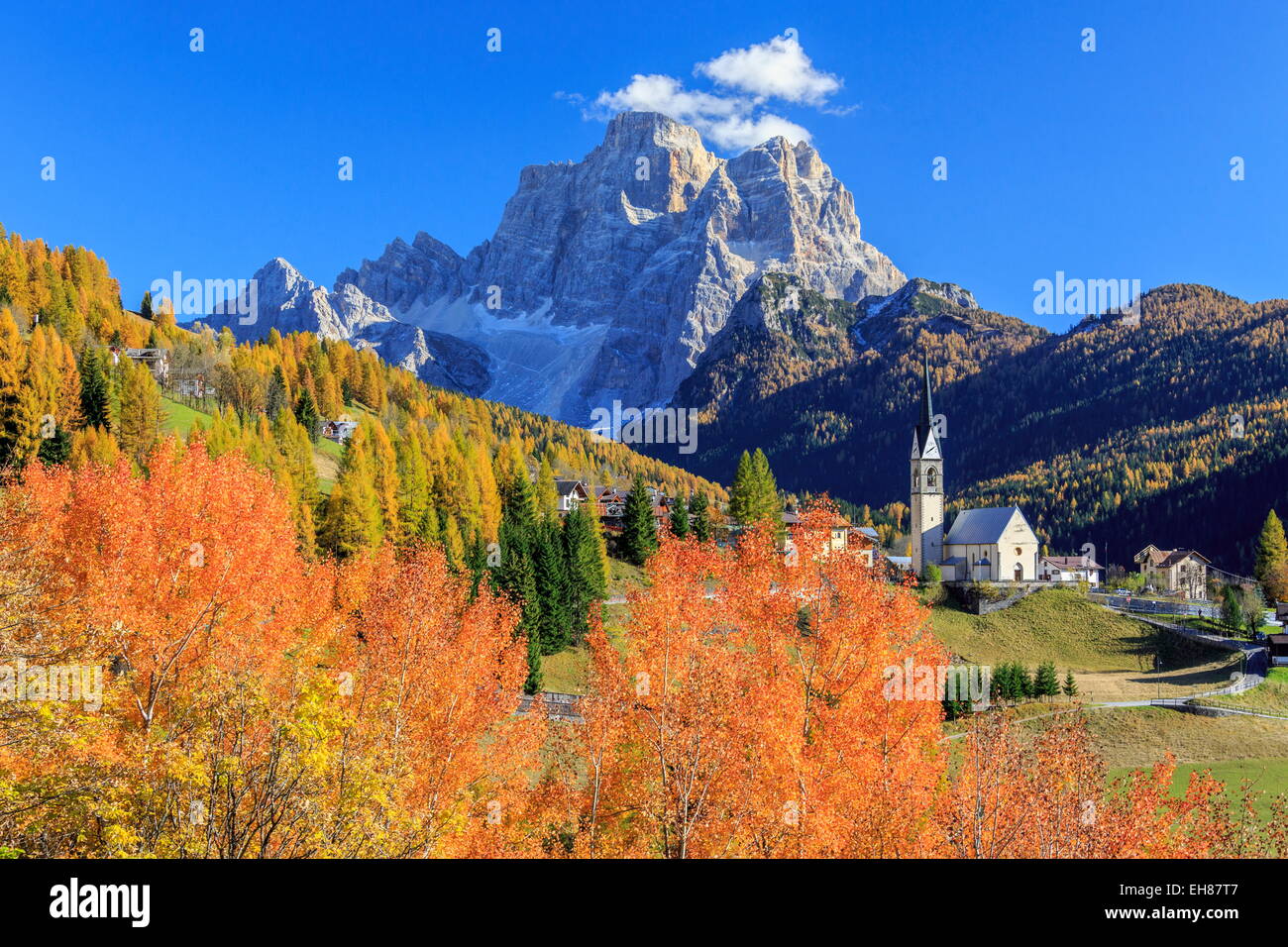 Red and orange trees with the tiny church of Selva di Cadore, in the Dolomites, Veneto, Italy Stock Photo