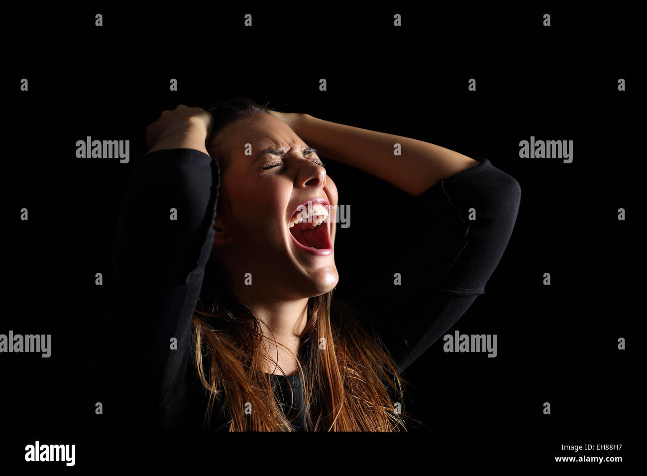 Depressed woman crying and shouting desperately isolated in a black background Stock Photo