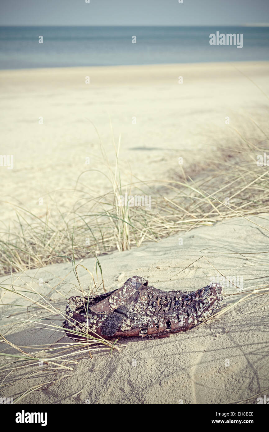 Retro filtered photo of an old weathered shoe washed up on beach. Stock Photo