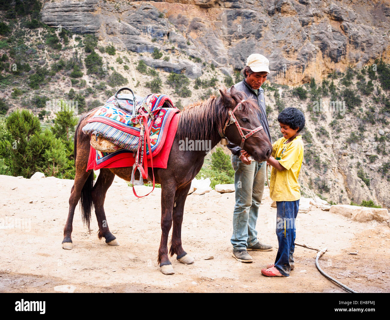 A young boy working at a remote roadside tea house in Bhena, Mustang, Nepal, greets a horse and its rider. Stock Photo