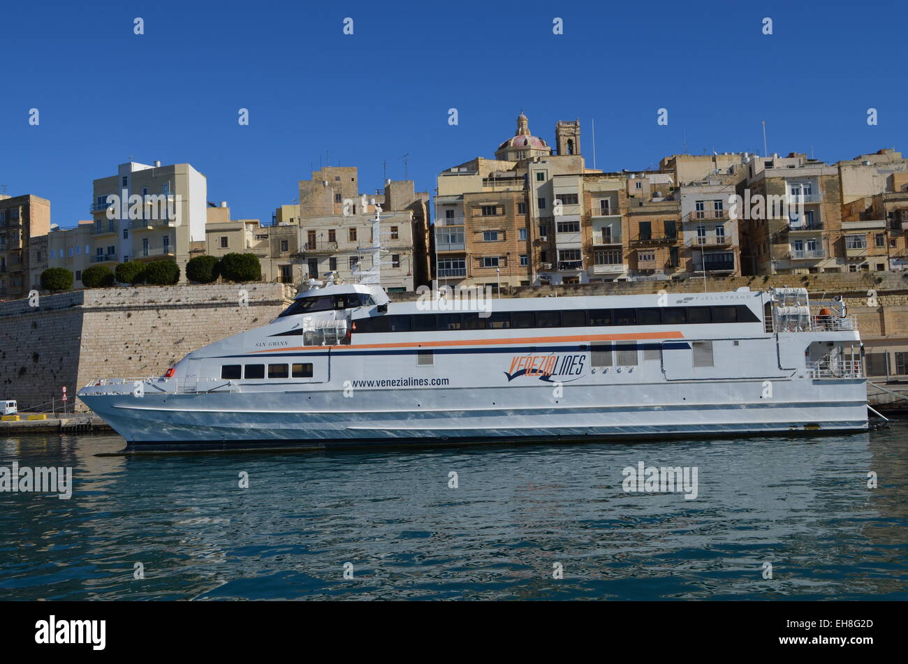 Continuing the trip around the Harbour of Malta we pass a number of boats that are tied up there. Above them looms Valletta. Stock Photo