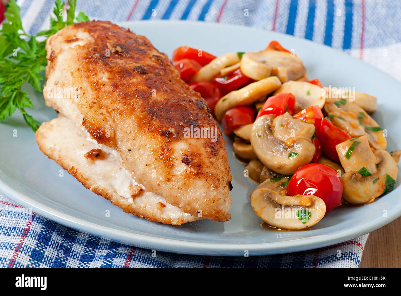 Chicken fillet in crispy breadcrumbs garnished with mushrooms and tomatoes Stock Photo