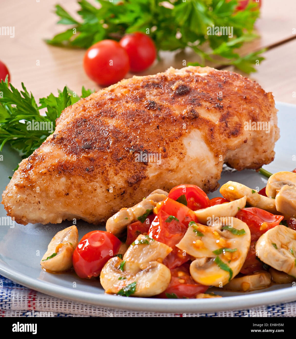 Chicken fillet in crispy breadcrumbs garnished with mushrooms and tomatoes Stock Photo