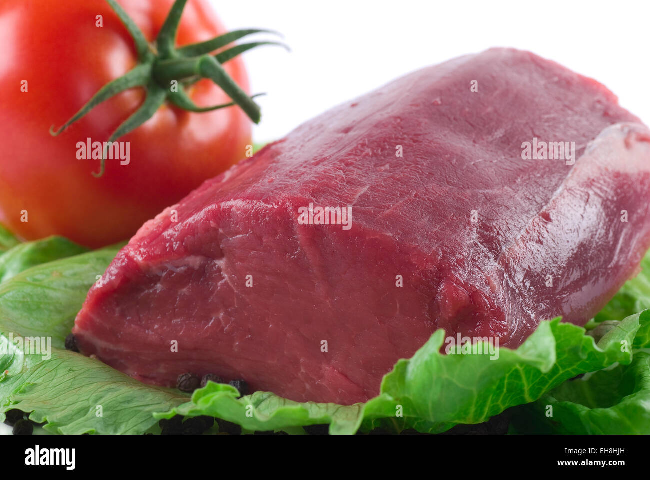 Fillet of beef on a iceberg lettuce leaf. Beef tomato in the background. Stock Photo