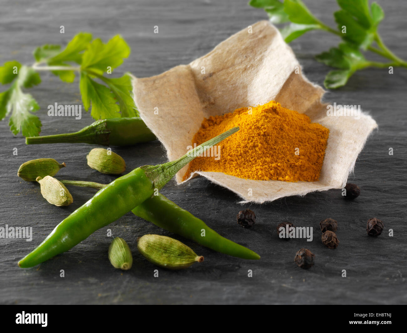 Fresh green birdseye chillies with ground turmeric & coriander leaves Indian spices composed arrangement Stock Photo