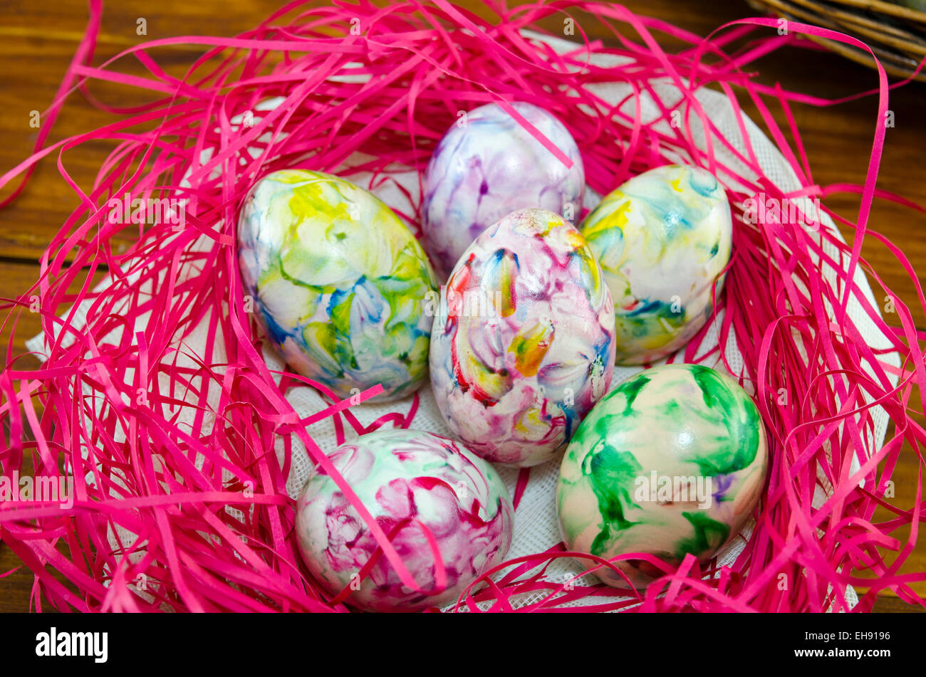 Colorful and painted eggs in a pink nest on a wooden table Stock Photo