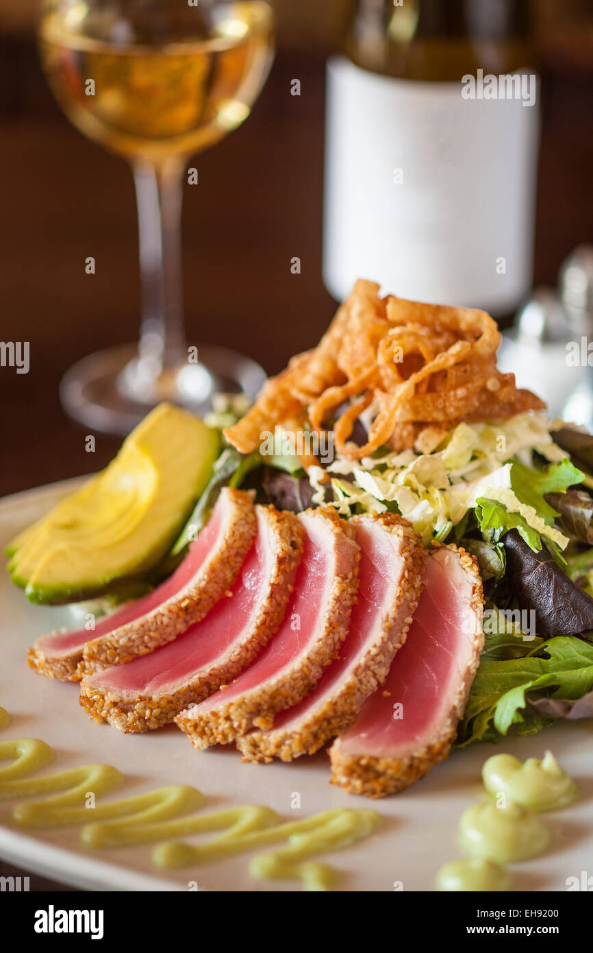 Sesame Crusted Seared Ahi with Baby Greens, Napa Cabbage, Avocado, Wonton Crisps, Soy Ginger Dressing, Wasabi Aioli and a glass Stock Photo