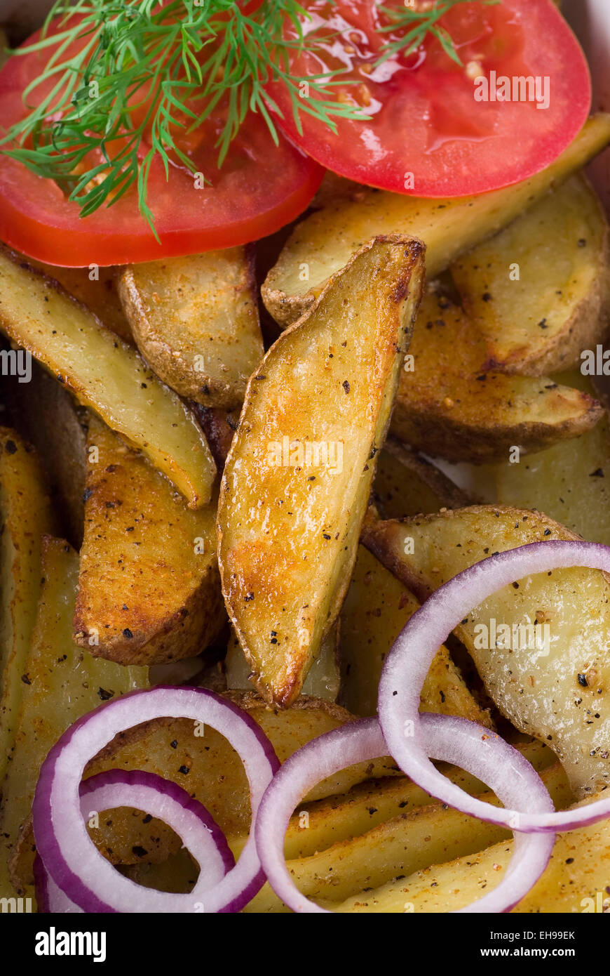 Roasted potato wedges, spanish onion and tomato. Stock Photo