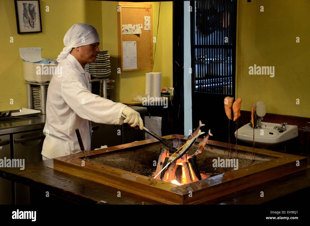 Japanese chef in kitchen grills fish on indoor coal fire Tokyo Japan