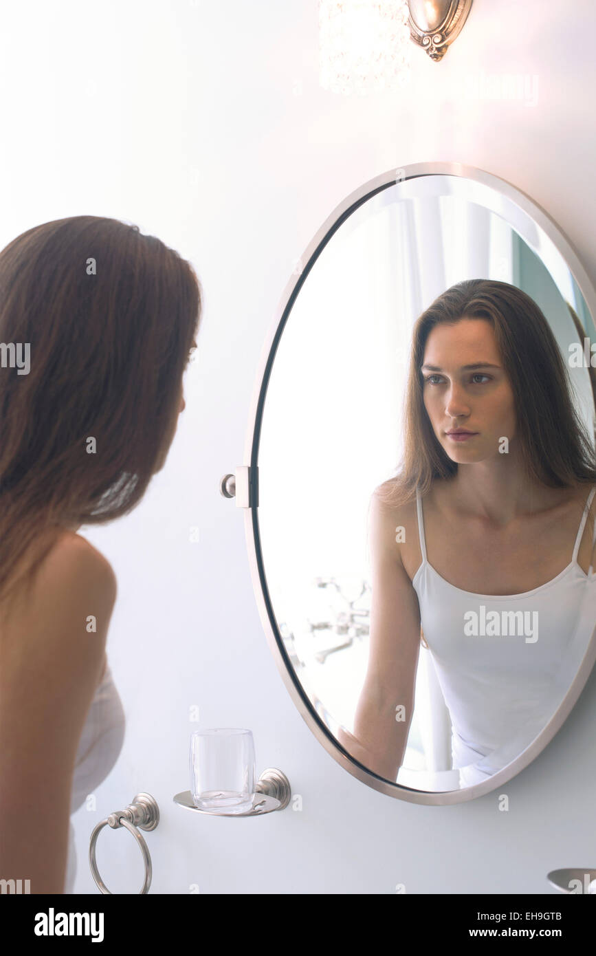 Woman looking at self in bathroom mirror Stock Photo