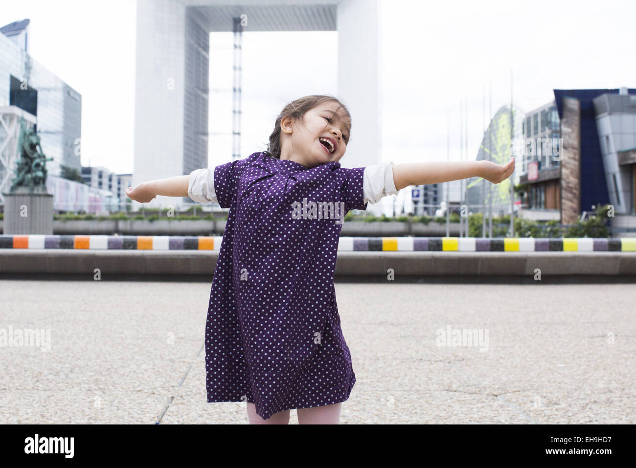 Little girl standing with her head back and arms outstretched in front of the Grande Arche, Paris, France Stock Photo