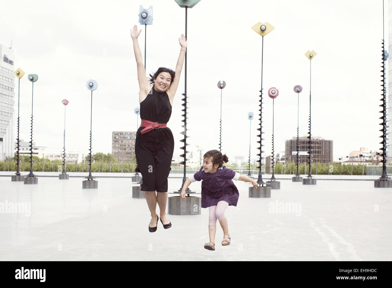Mother and daughter jumping in front of whimiscal sculptures, La Defense, Paris, France Stock Photo