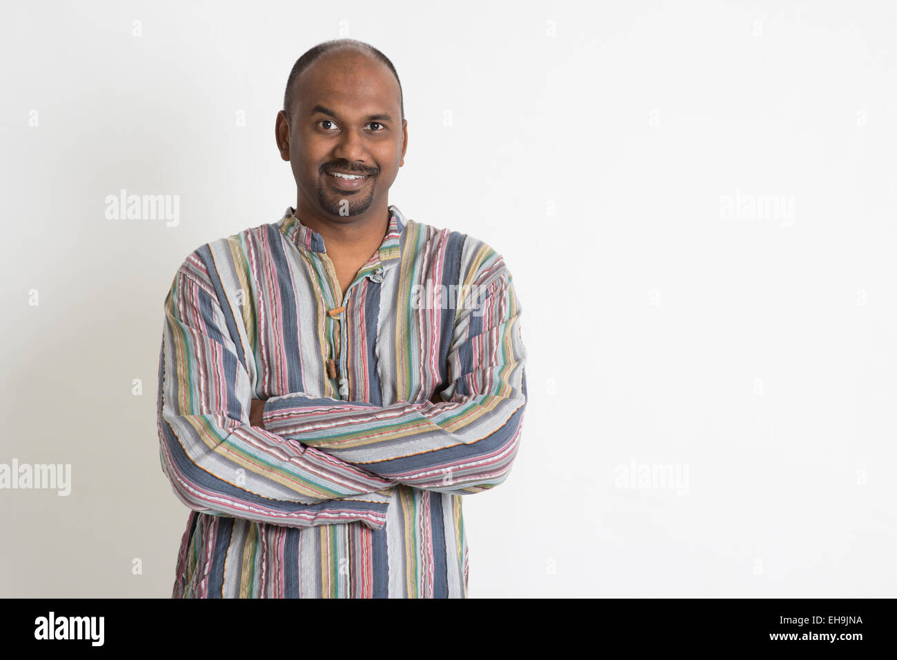 Portrait of smiling Indian man arms crossed on plain background with ...