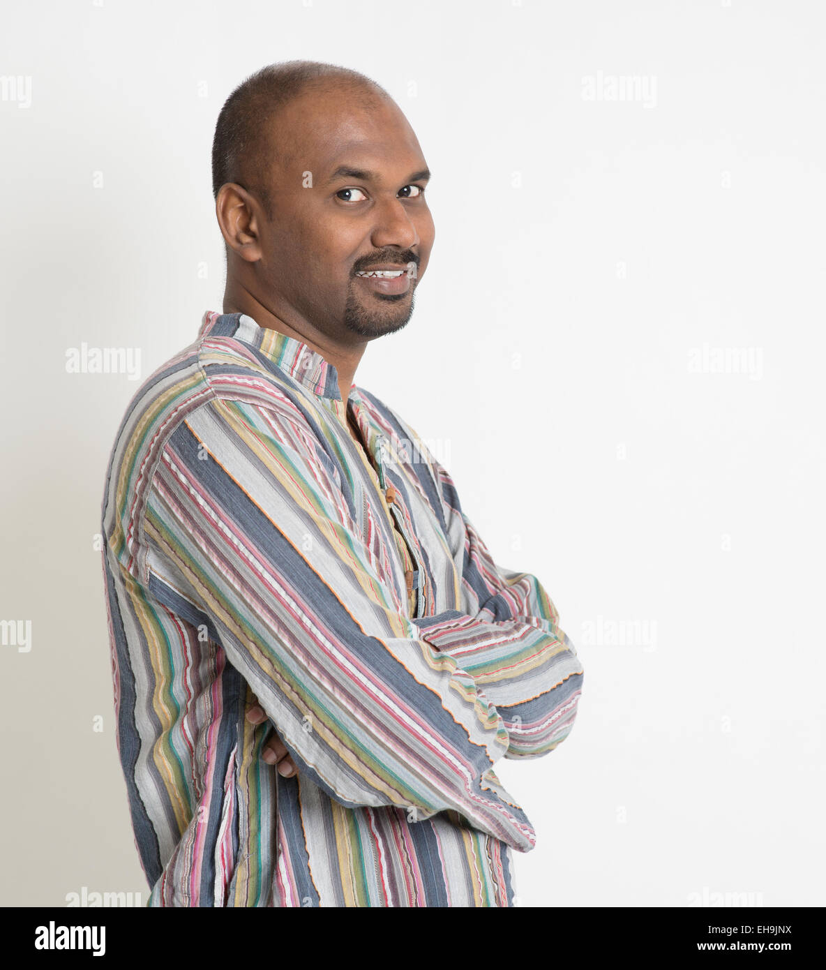 Portrait of smiling Indian man arms crossed looking at camera on plain ...