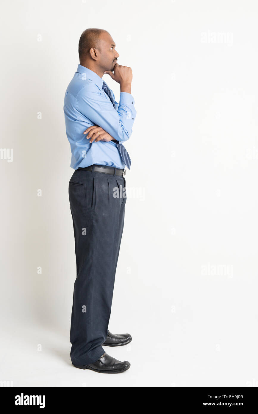 Profile view of full body Indian businessman hand on chin looking up at  blank copy space, standing on plain background with shad Stock Photo - Alamy