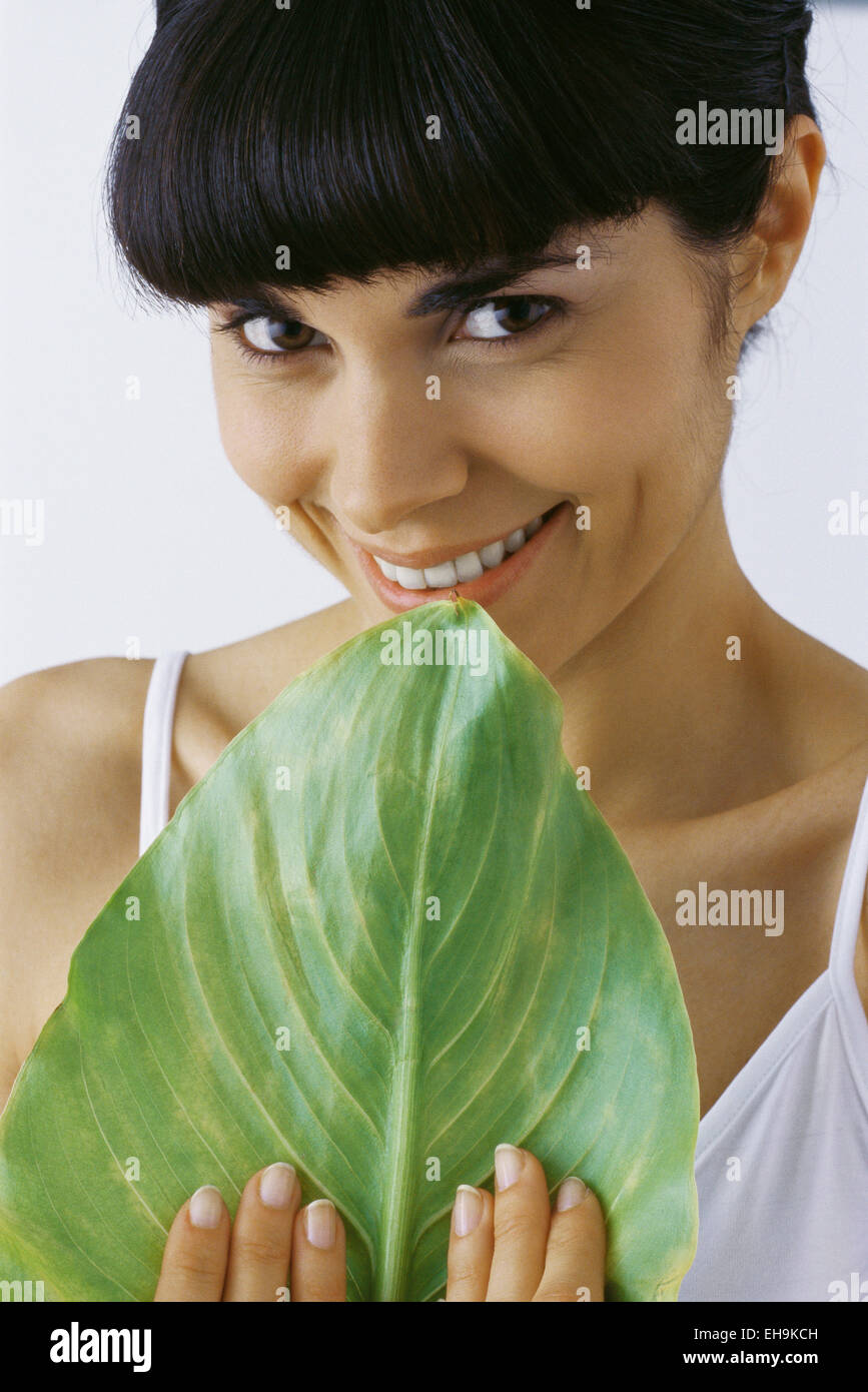 Young woman holding leaf, smiling, portrait Stock Photo