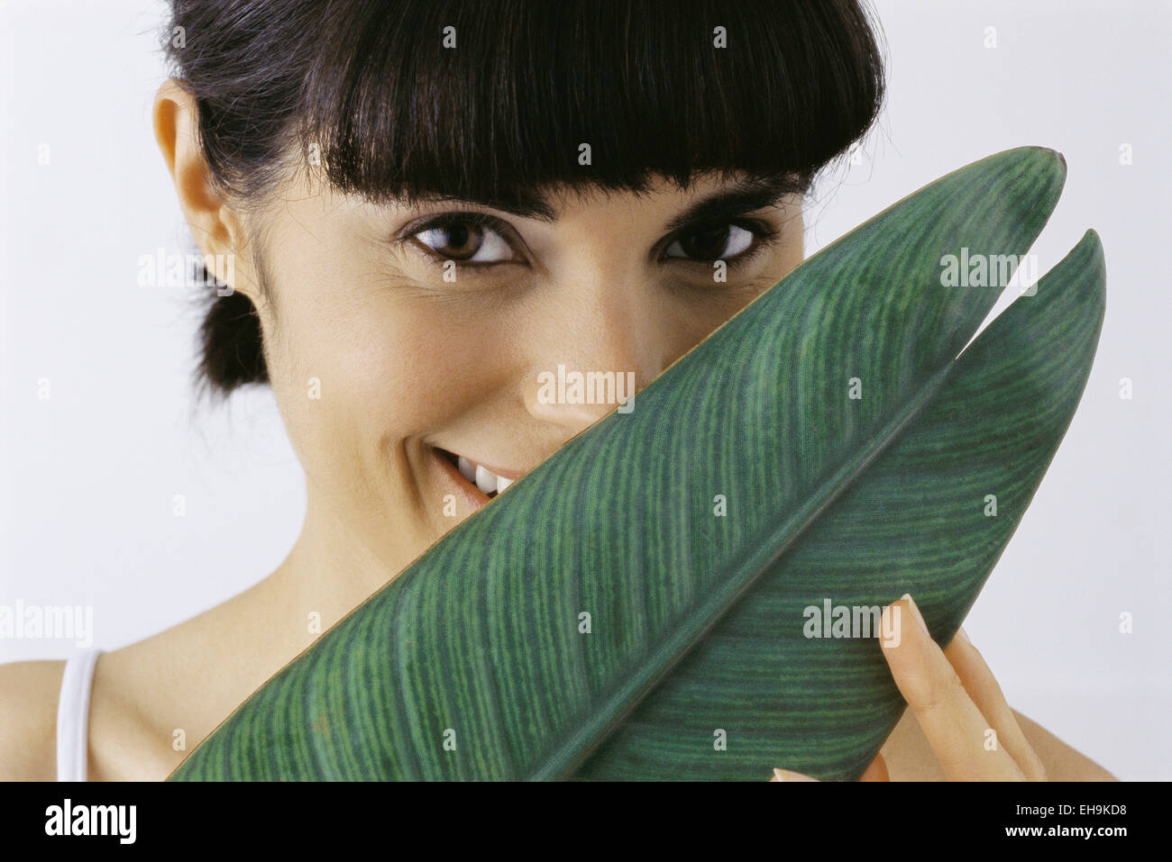 Young woman holding leaf in front of face, smiling, portrait Stock ...