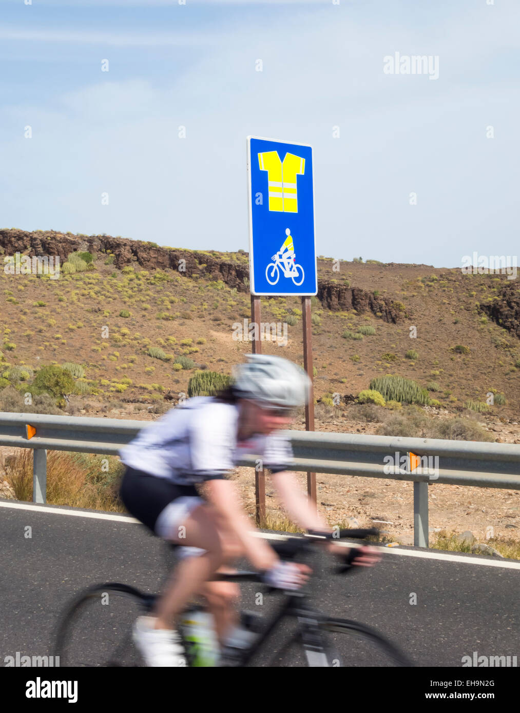 Cyclist passing sign on mountain road on Gran Canaria indicating obligatory use of high visibility jacket. Stock Photo