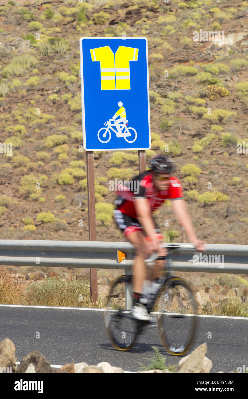 Cyclist passing sign on mountain road on Gran Canaria indicating obligatory use of high visibility jacket Stock Photo