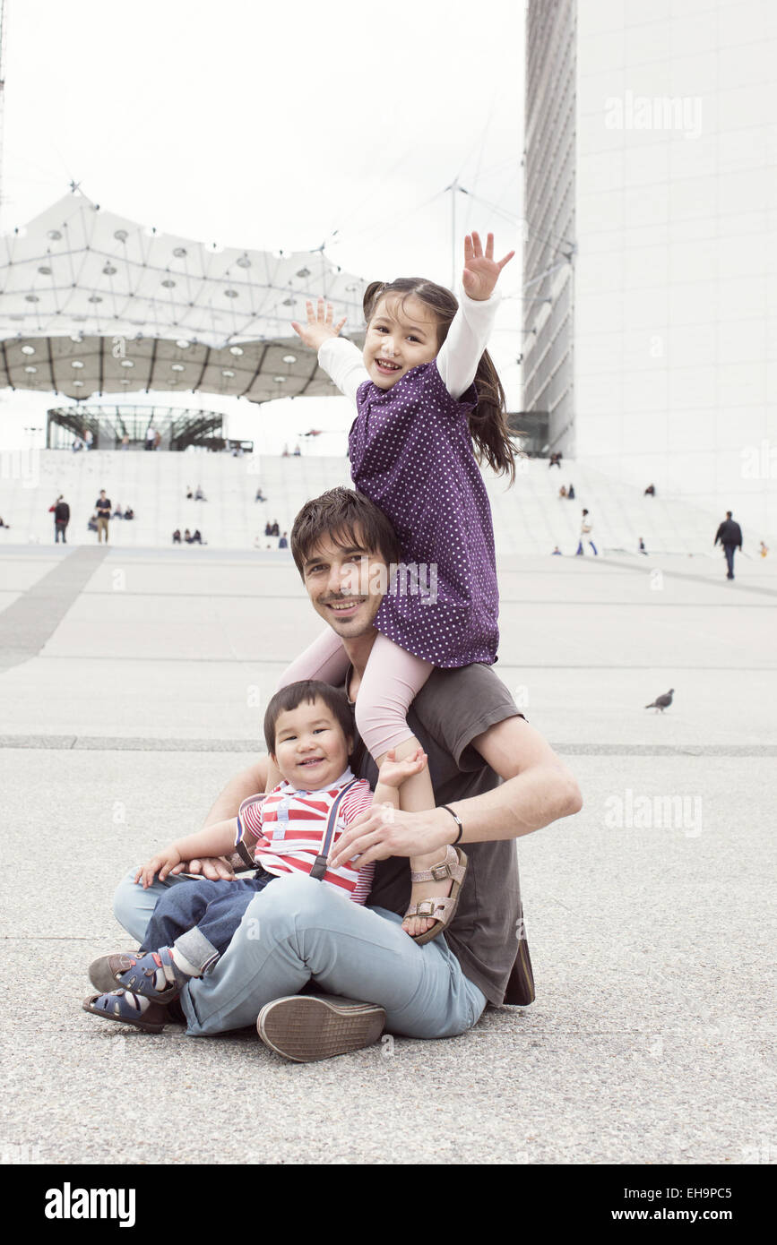 Father sitting on the ground with two children in city square Stock Photo