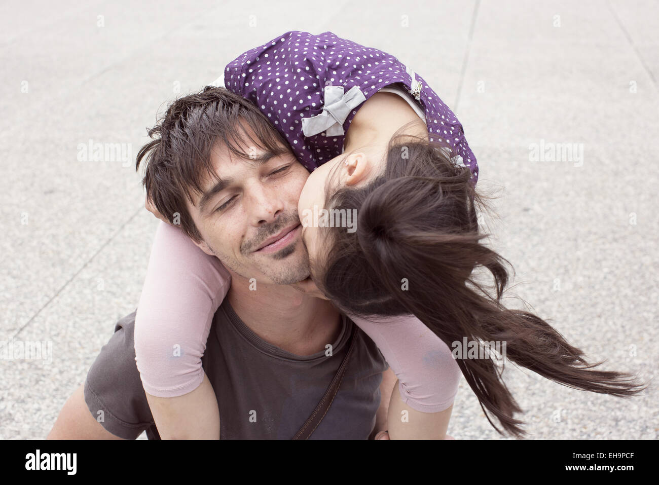 Little girl riding on father's shoulders, kissing his cheek Stock Photo
