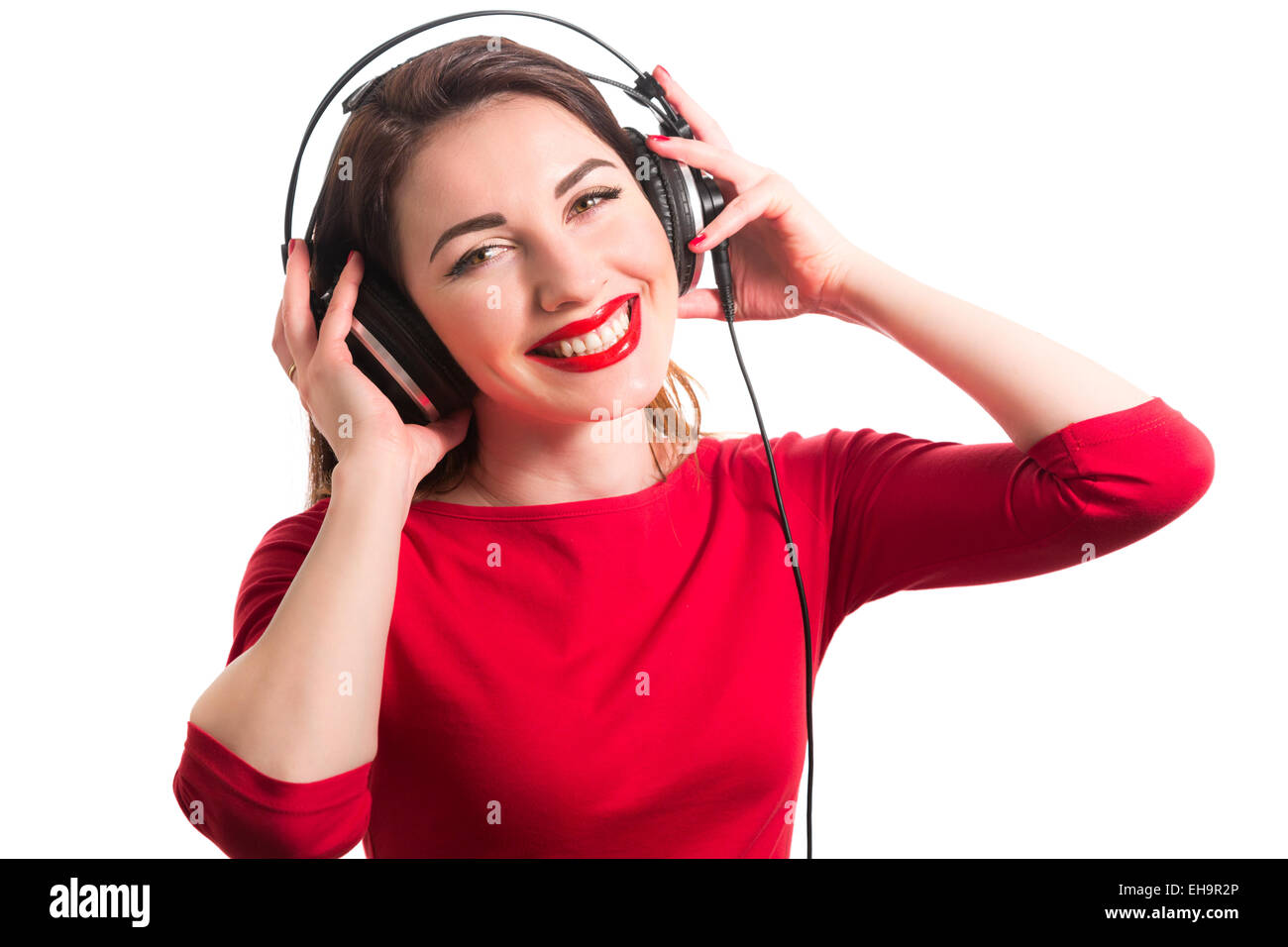 Girl in long-sleeve t-shirt wearing red lipstick touching big headphones listening to music smiling and looking at camera isolat Stock Photo