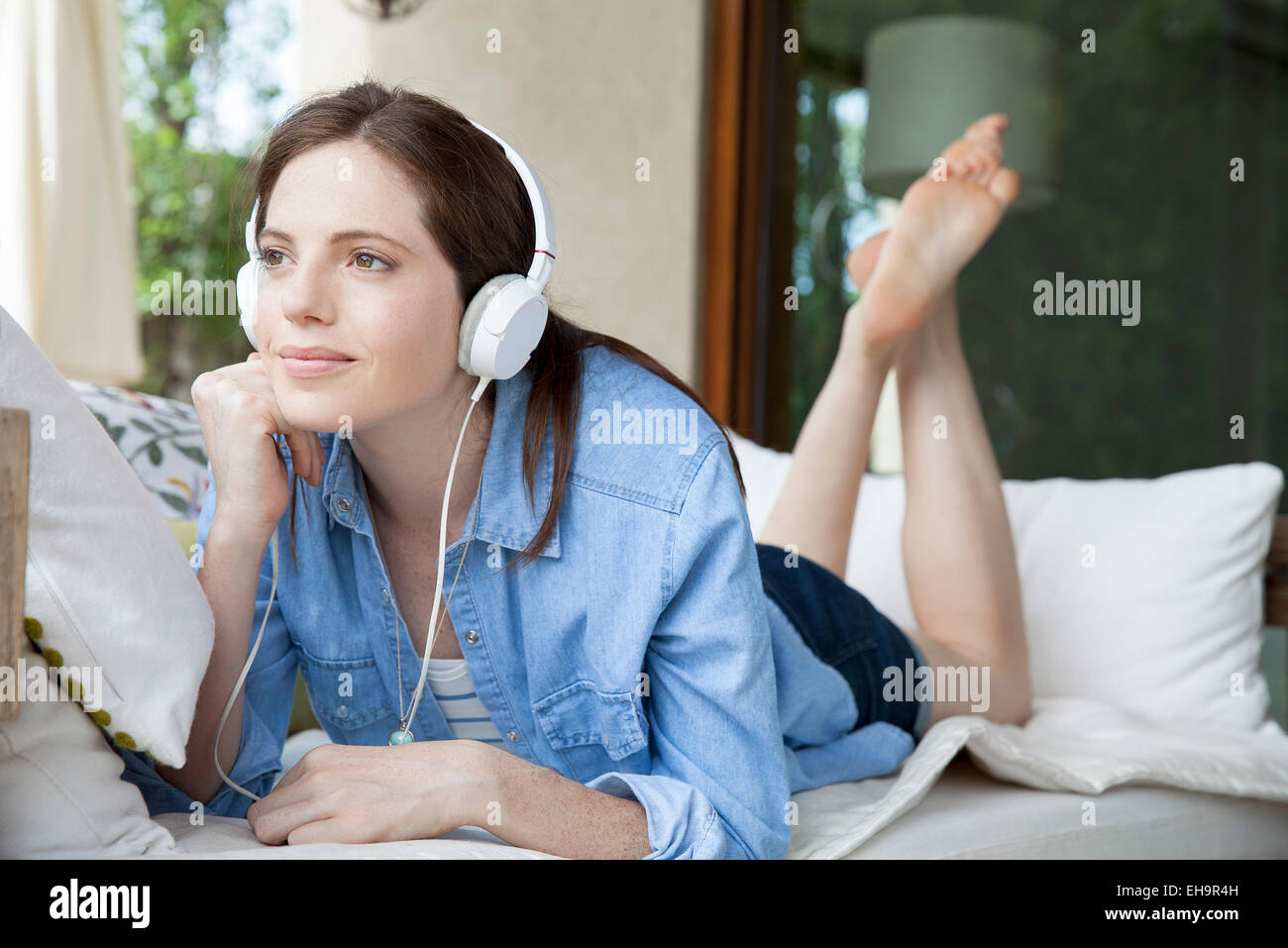 Young woma lying on stomach, listening to headphones Stock Photo