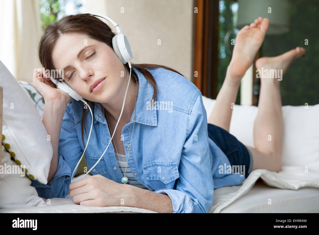Young woma lying on stomach, listening to headphones with eyes closed Stock Photo