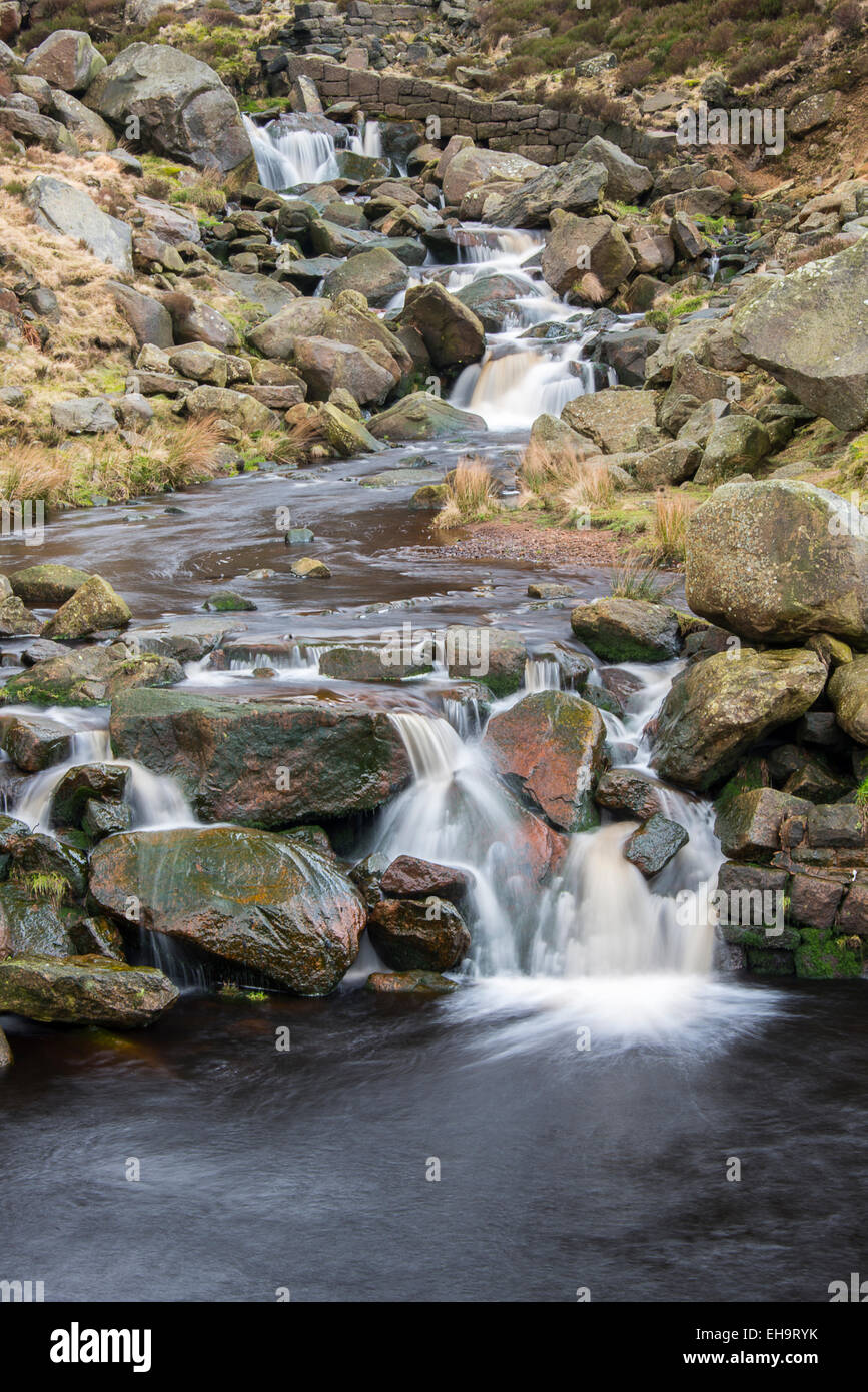 A small stream tumbling over fallen millstone grit blocks in a valley in the Northern Peak District area of Saddleworth close to Stock Photo