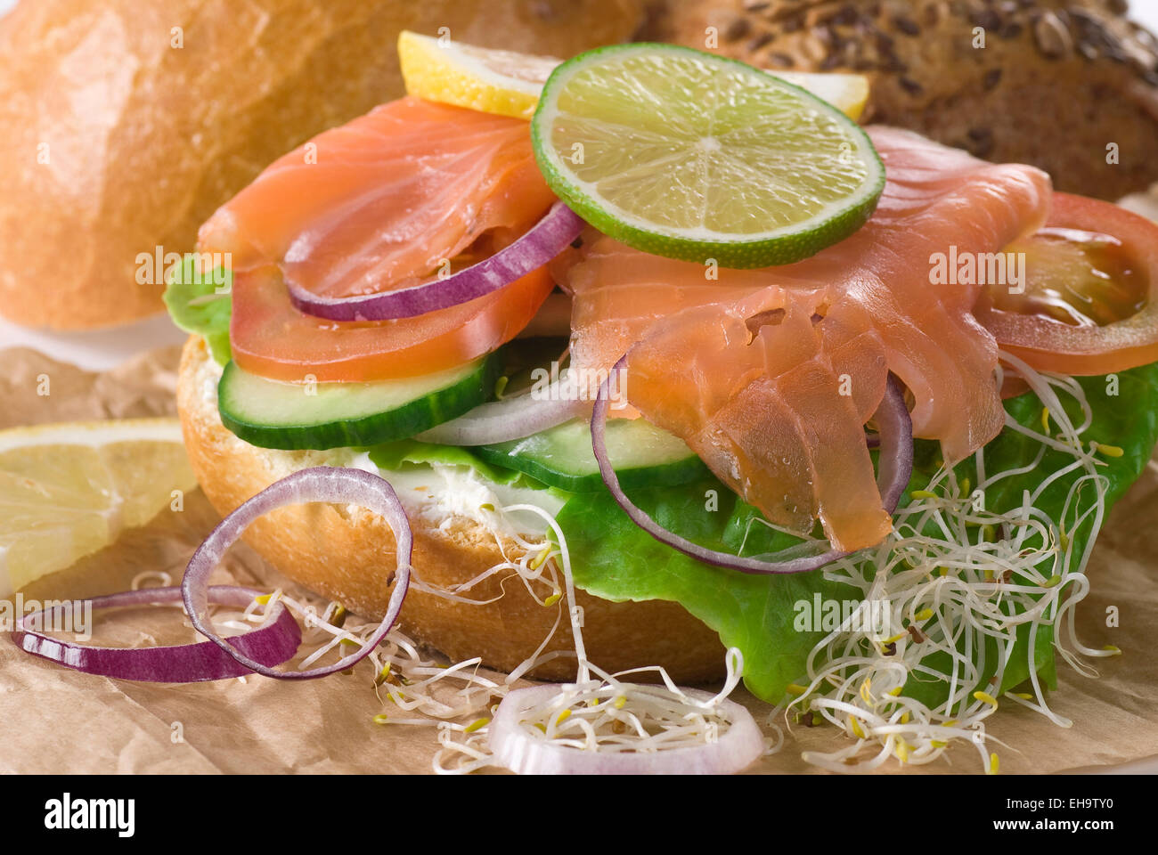 Bread with cream cheese, lettuce, cucumber, smoked salmon, onion, tomato, lime and lemon. Stock Photo