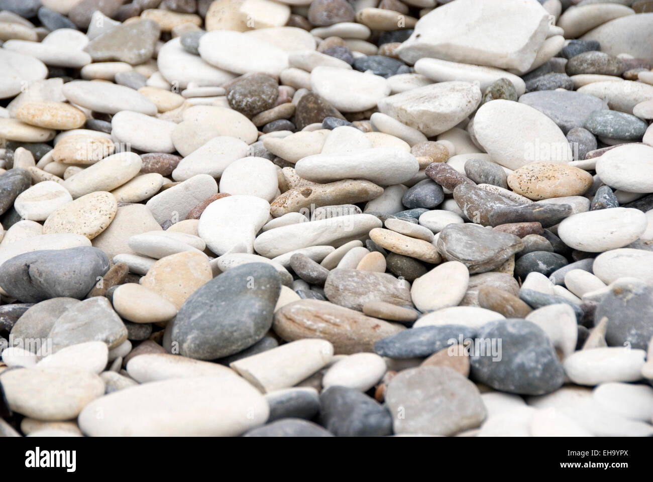 Rounded pebbles in shades of grey, blue, white, cream and orange scatter the beach at Bridlington, UK Stock Photo