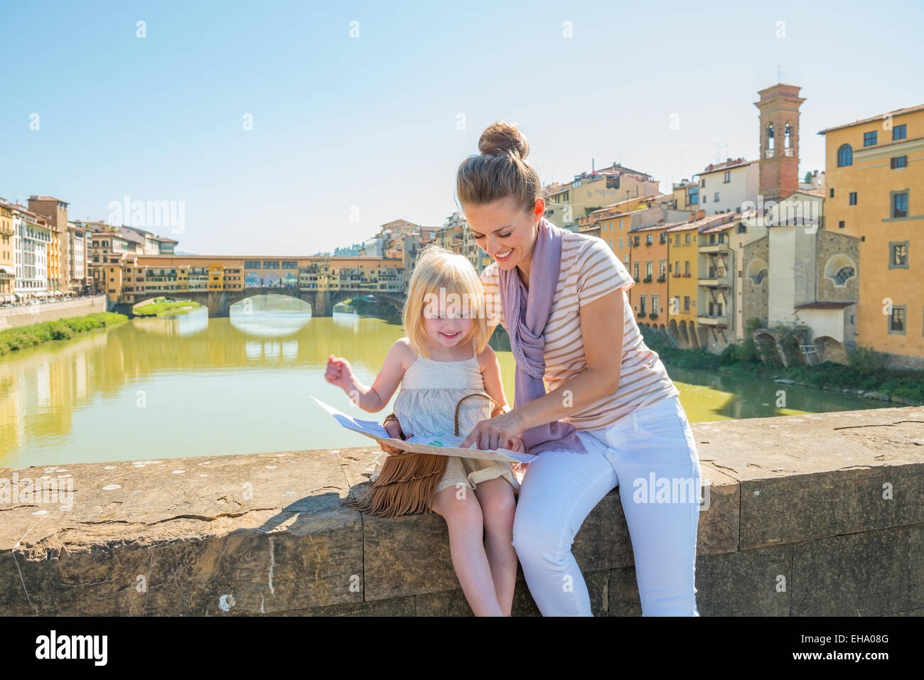Mother and baby girl sitting on bridge overlooking ponte vecchio in florence, italy and looking at map Stock Photo