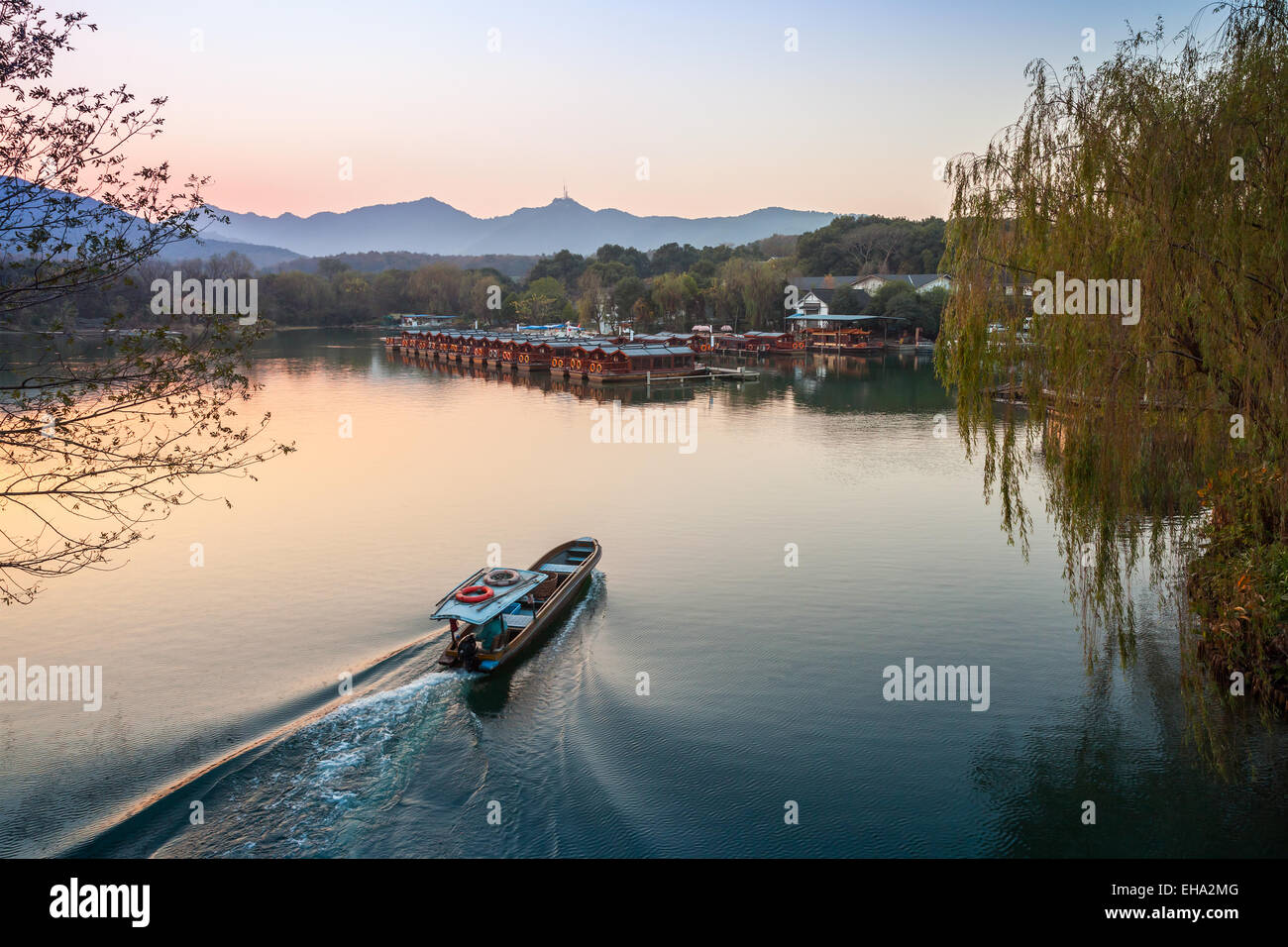 Small Chinese fishing boat with boatman goes to the West Lake coast. Famous park in Hangzhou city center, China Stock Photo