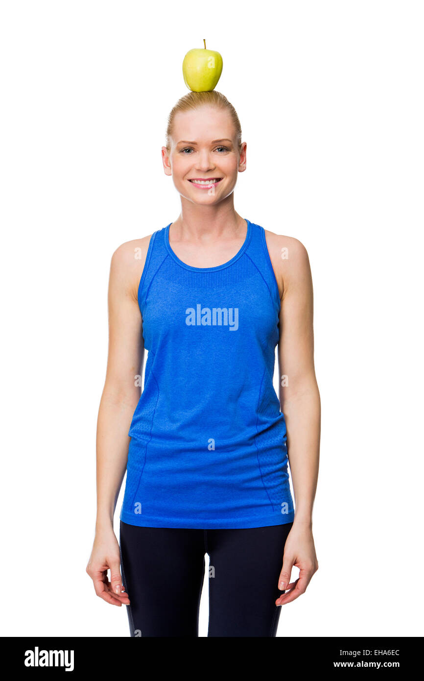 smiling woman wearing fitness clothing holding an apple on her head Stock Photo