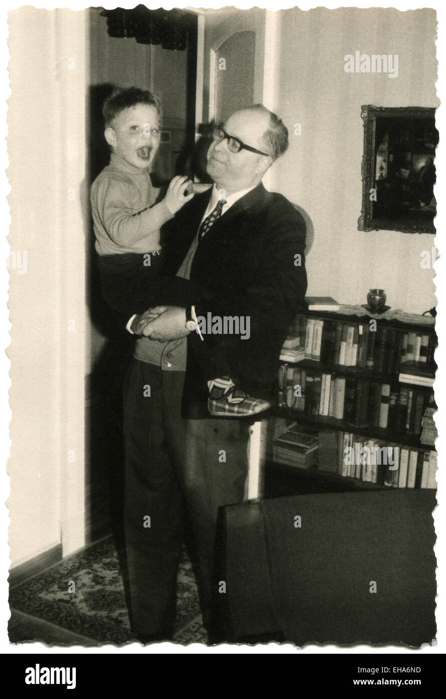 Germany. 9th Mar, 2015. CIRCA 1970: Bald businessman wearing glasses and a business suit is holding a little boy in shorts. He is standing in the living room © Igor Golovniov/ZUMA Wire/ZUMAPRESS.com/Alamy Live News Stock Photo