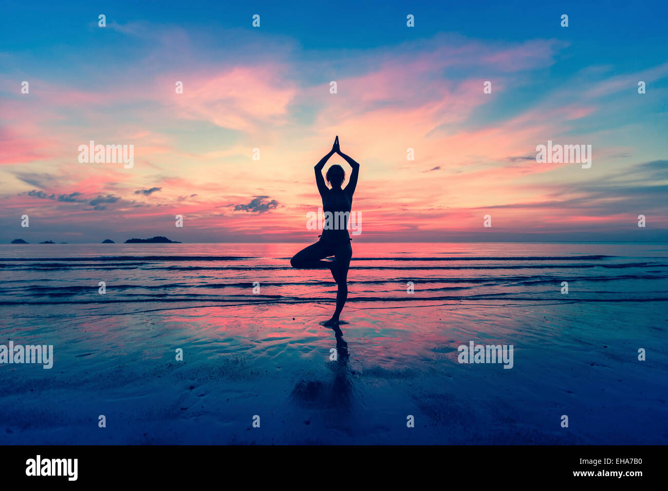 Silhouette of woman standing at yoga pose on the beach during an ...