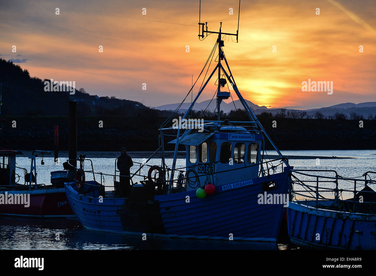 Donegal, Ireland. 10th March, 2015. Weather: A man stands on the ‘Ros Eireann’ fishing boat as the sun sets over Lough Swilly at Fahan, County Donegal. Widespread showers are forecast for Donegal on Wednesday. Credit:  George Sweeney/Alamy Live News Stock Photo