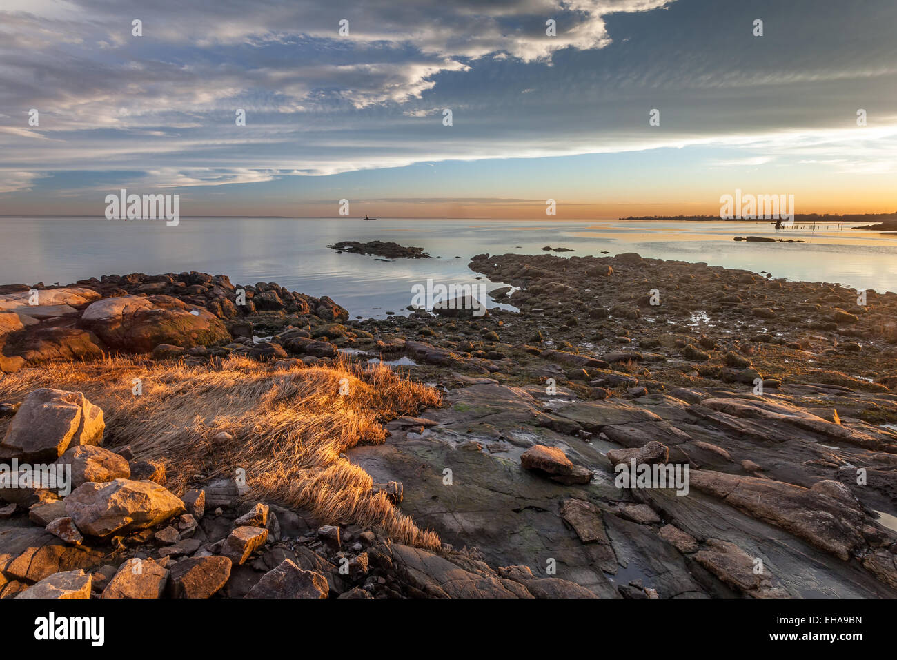 A rocky and grassy beach at sunset with a partially blue sky and NYC off in the far distance. Stock Photo