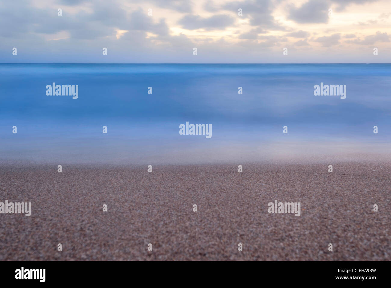 Minimalist view from the Florida beach of a flat calm ocean at sunrise with fluffy clouds in the sky. Stock Photo