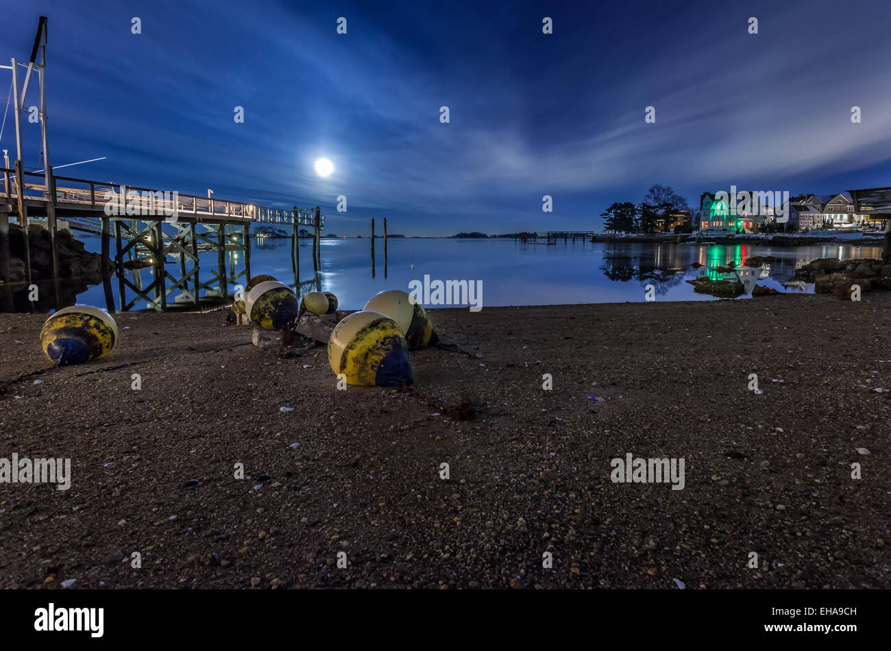 Buoys and floats on the shore by a deck under a blue moonlit sky at night. Stock Photo