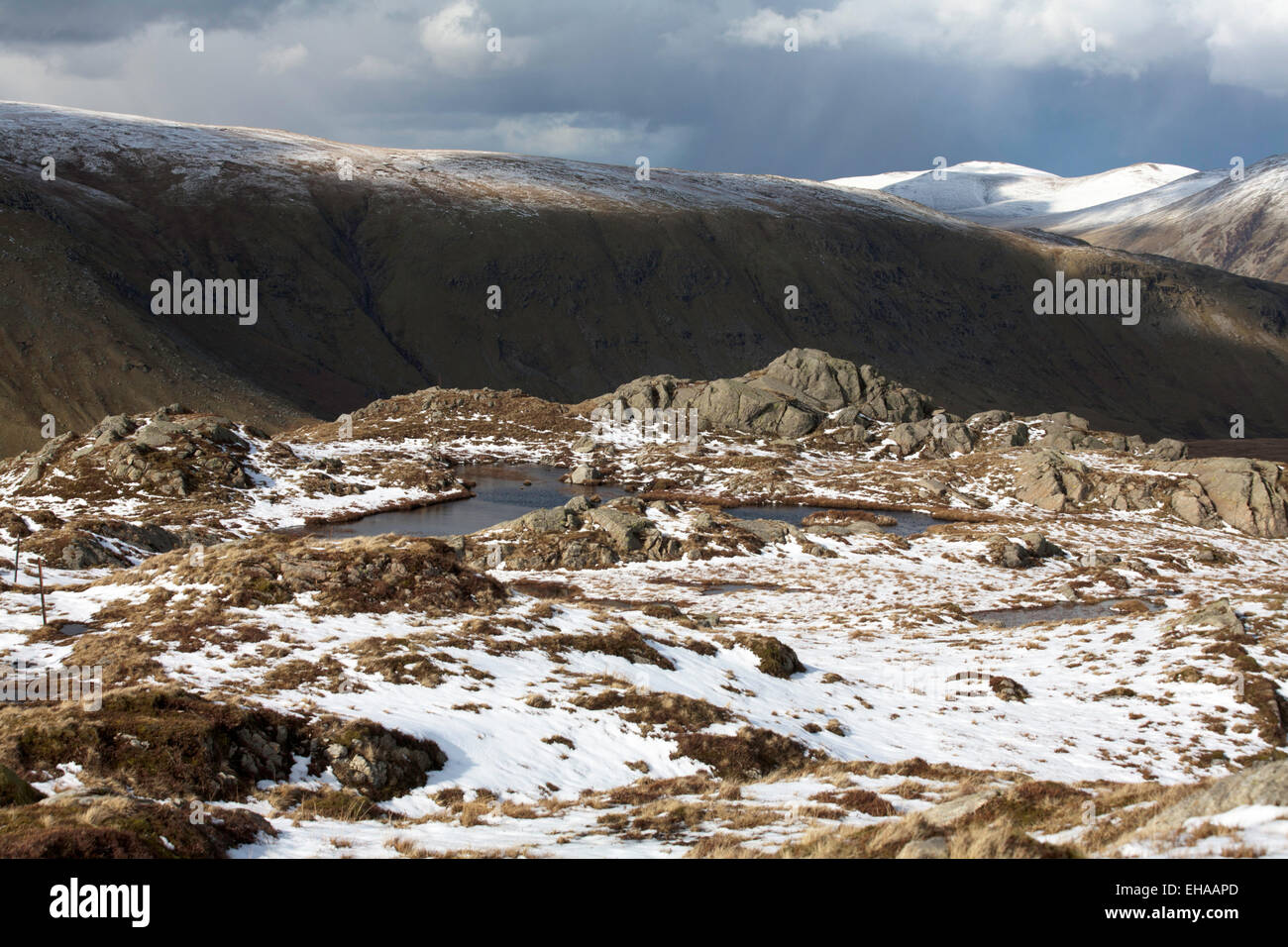 Storm & shower clouds passing over  snow capped summit of Helvellyn from near Ash Crags on High Raise above Grasmere Cumbria Stock Photo