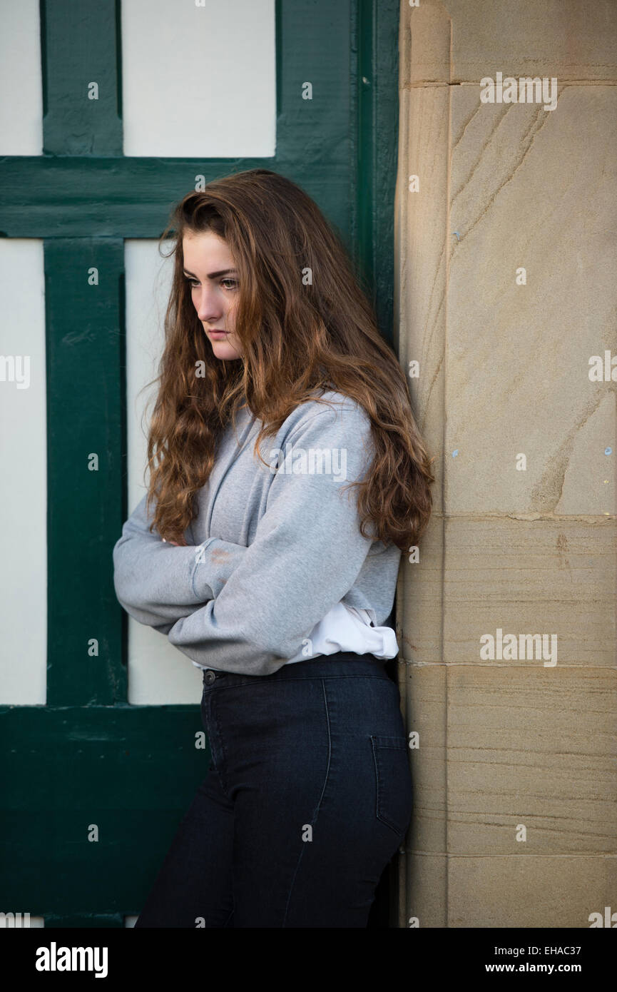 A moody young 13 14 15 year old teenage girl with long brown hair outdoors  alone by herself  UK Stock Photo