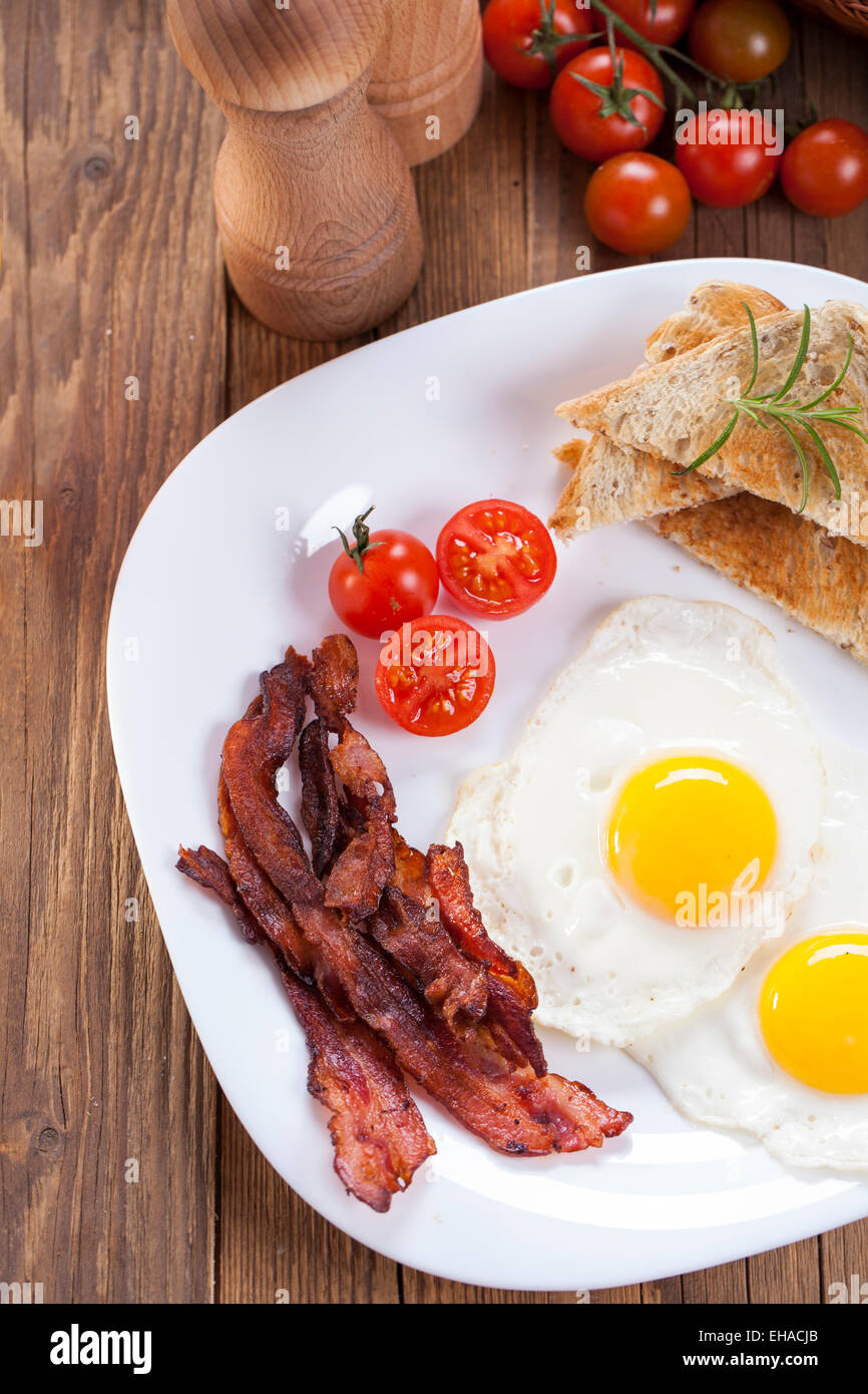 Fried egg and bacon on a plate with spices and vegetables. Studio shot