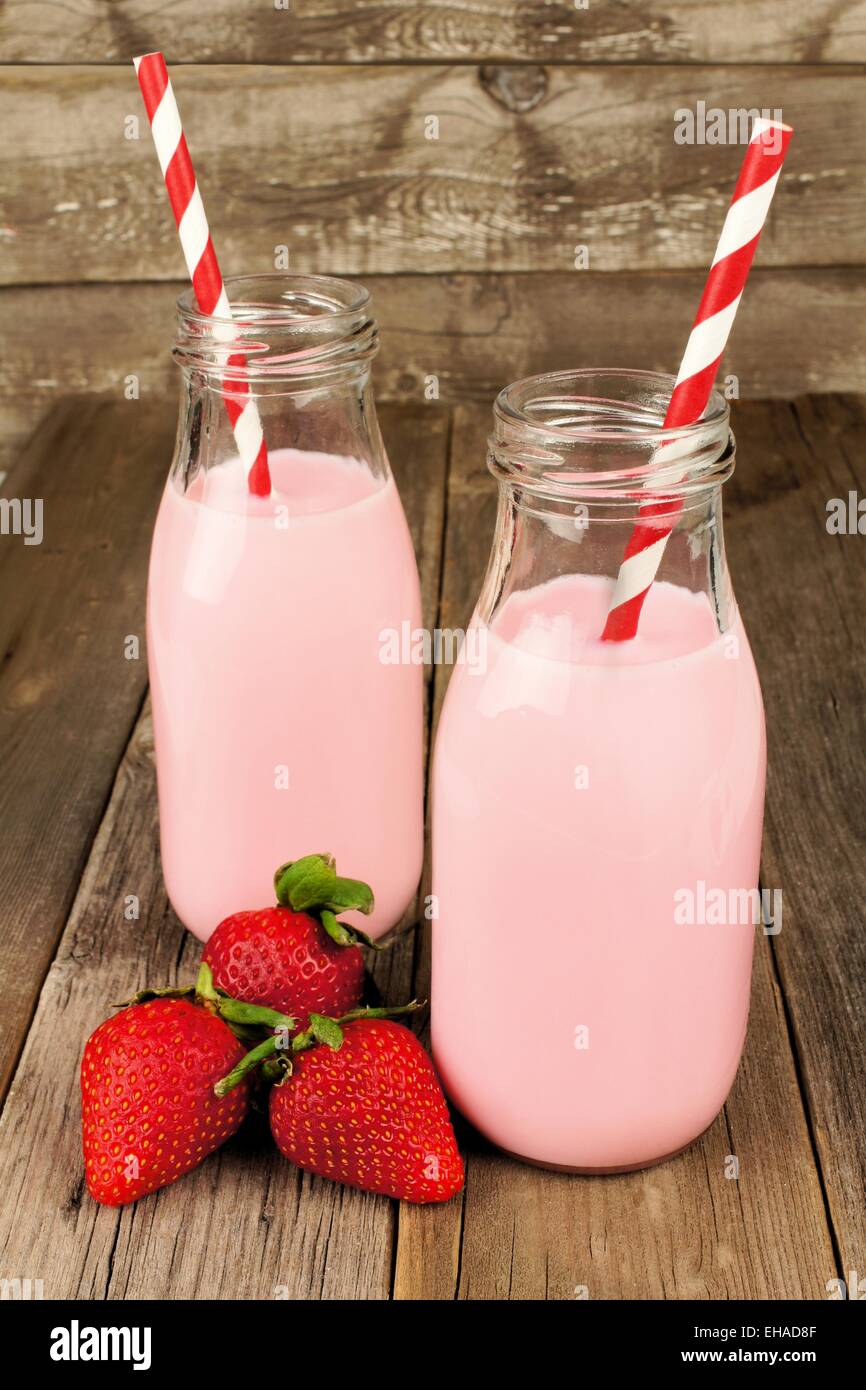Strawberry milk in traditional bottles with straws on old wood background Stock Photo
