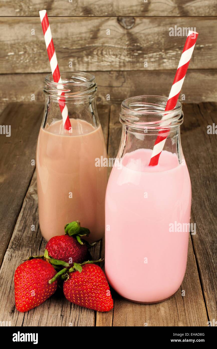 Strawberry and chocolate milk in traditional bottles with straws on old wood background Stock