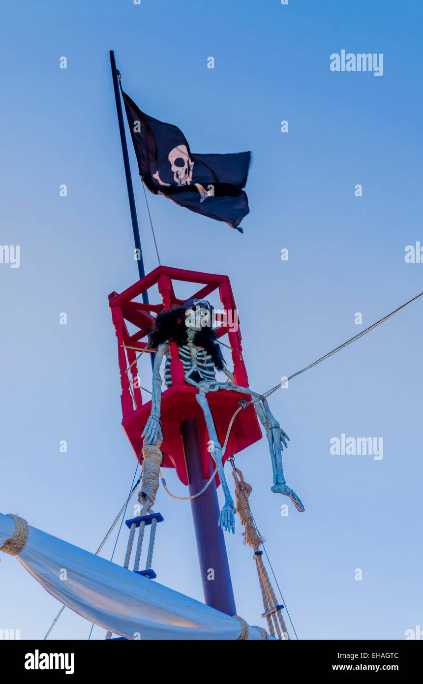 Skeleton in Davy Jones's locker. atop Pirate ship mast and Jo;lly Rodger flag,. Stock Photo