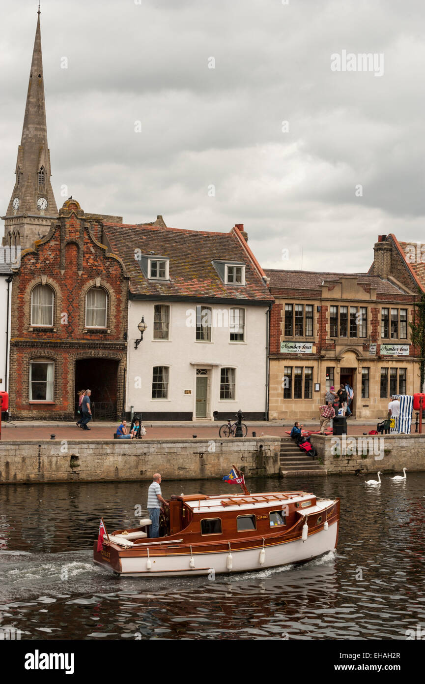 A wooden motor boat cruises along the River Ouse through the town of Saint Ives, Cambridgeshire. Stock Photo