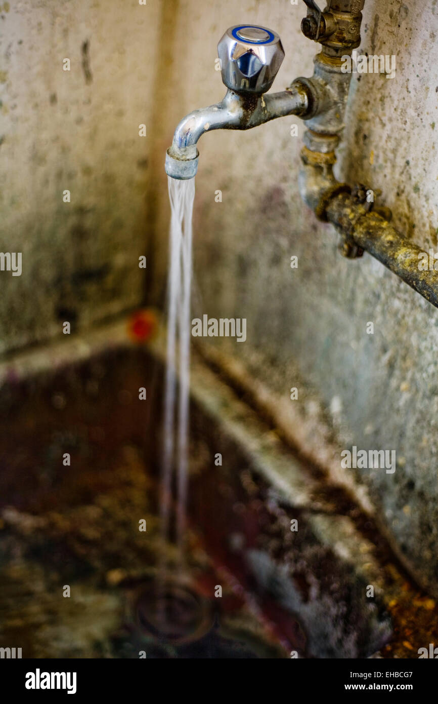 Water From The Faucet Flowing Into An Old Dirty Drain Stock Photo