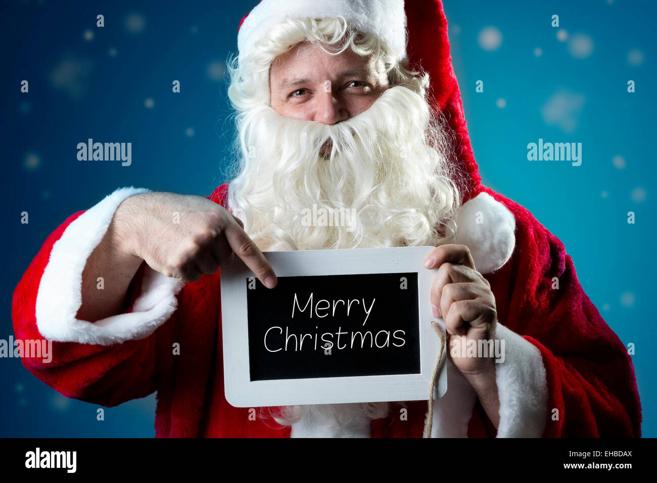Santa Claus pointing a finger on a blank slate with text Merry Christmas Stock Photo