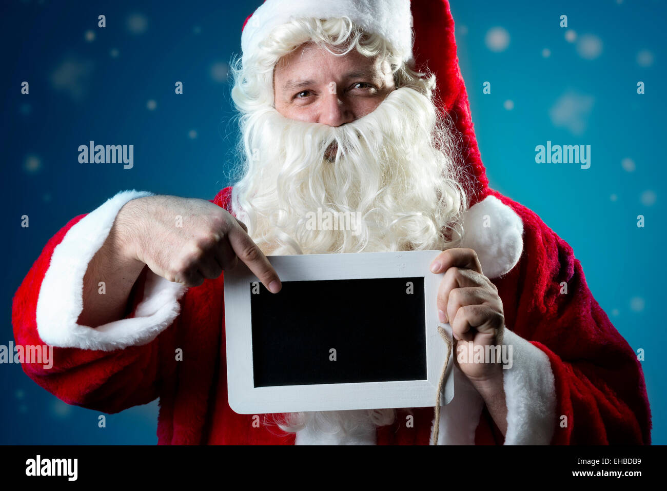 Image portrait of Santa Claus in red coat with snow pointing a finger on a blank slate Stock Photo